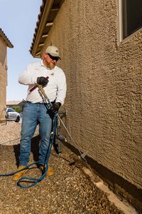 Technician performing liquid termite treatment to soil along foundation of home.